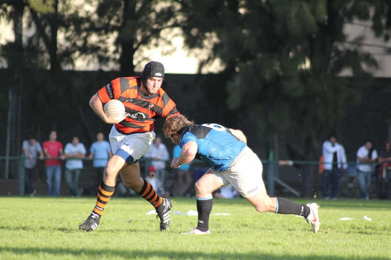 Jugador de Olivos corriendo con la pelota y esquivando un tackle