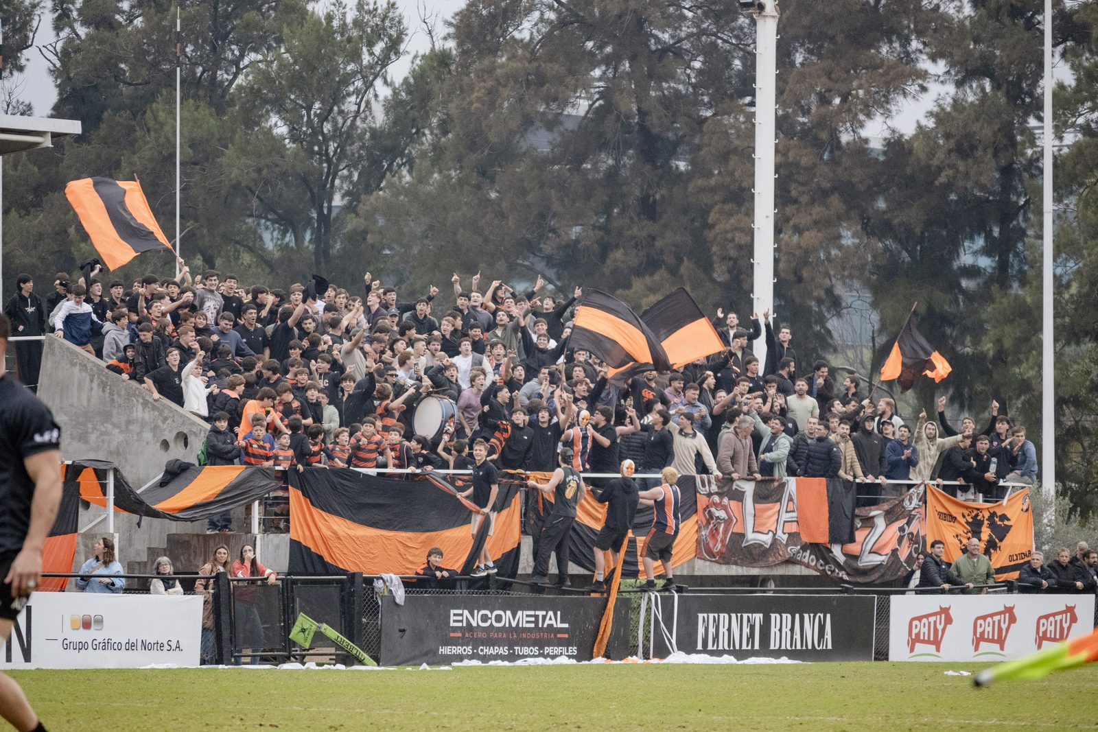 Hinchada de Olivos festejando en la tribuna del club con banderas naranjas y negras