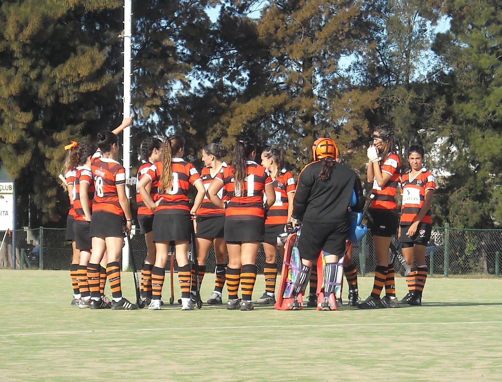 Jugadoras de hockey de Olivos reunidas en ronda en la cancha, con la arquera al centro